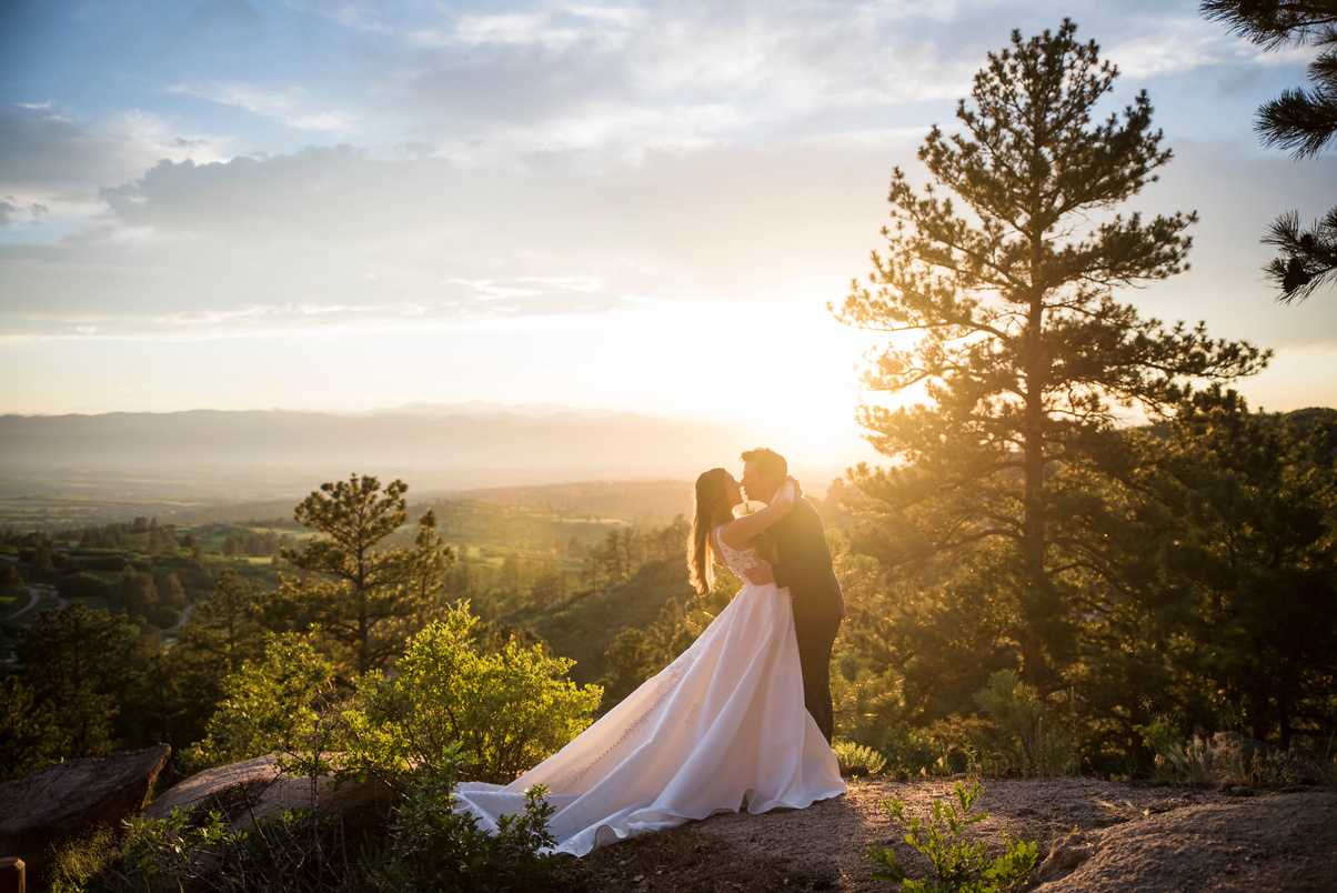 A bride and groom hug and look into each other's eyes standing on an overlook at Daniels Park at sunset.