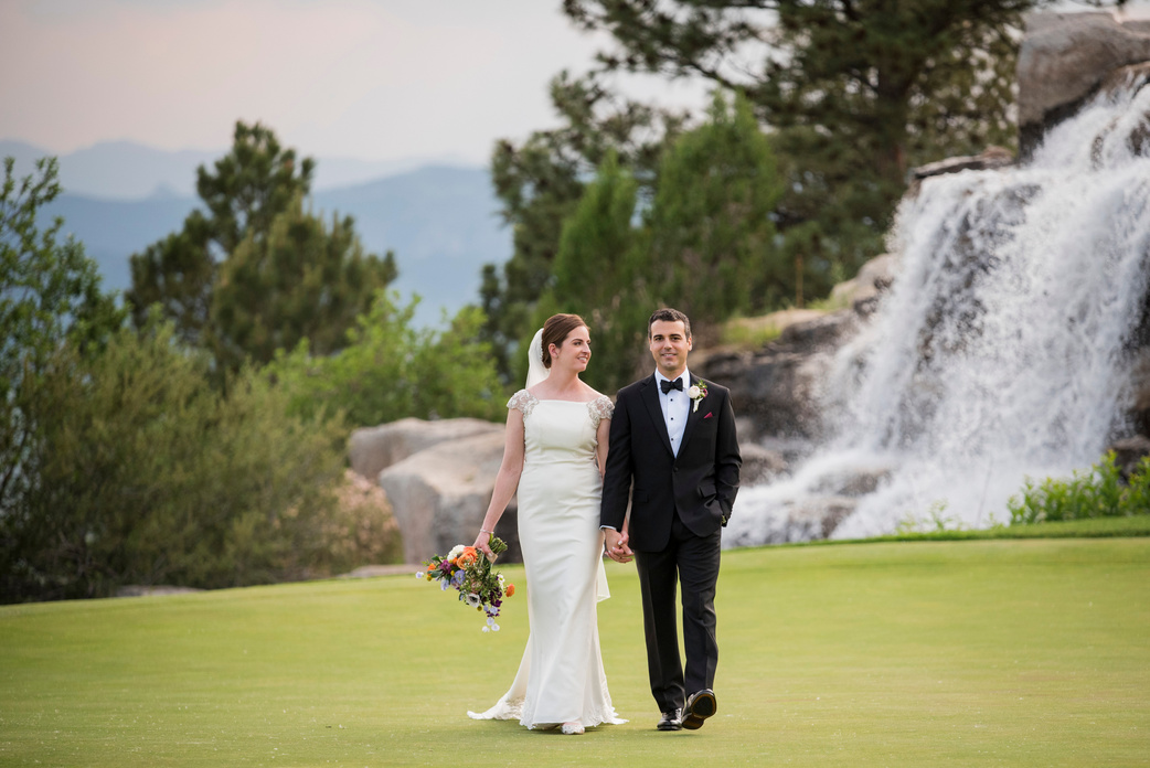 A bride and groom walk toward the camera holding hands on the golf course at The Sanctuary in Sedalia, Colorado.