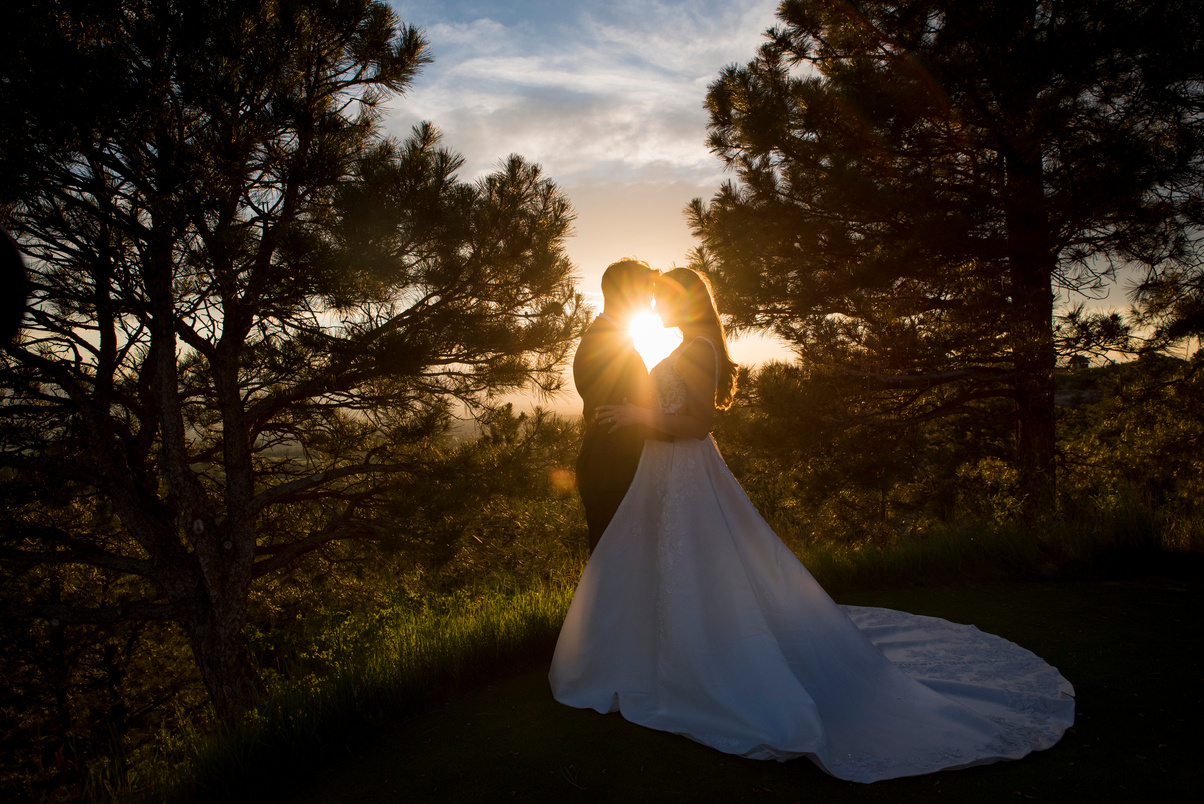 The bride and groom are silhouetted against the sun at sunset at The Sanctuary in Sedalia, Colorado.