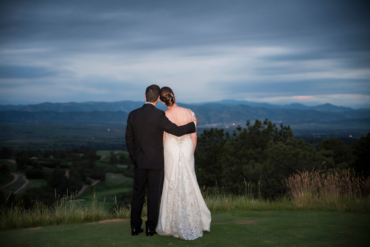 A bride and groom face away from the camera, looking out at the Colorado mountains.
