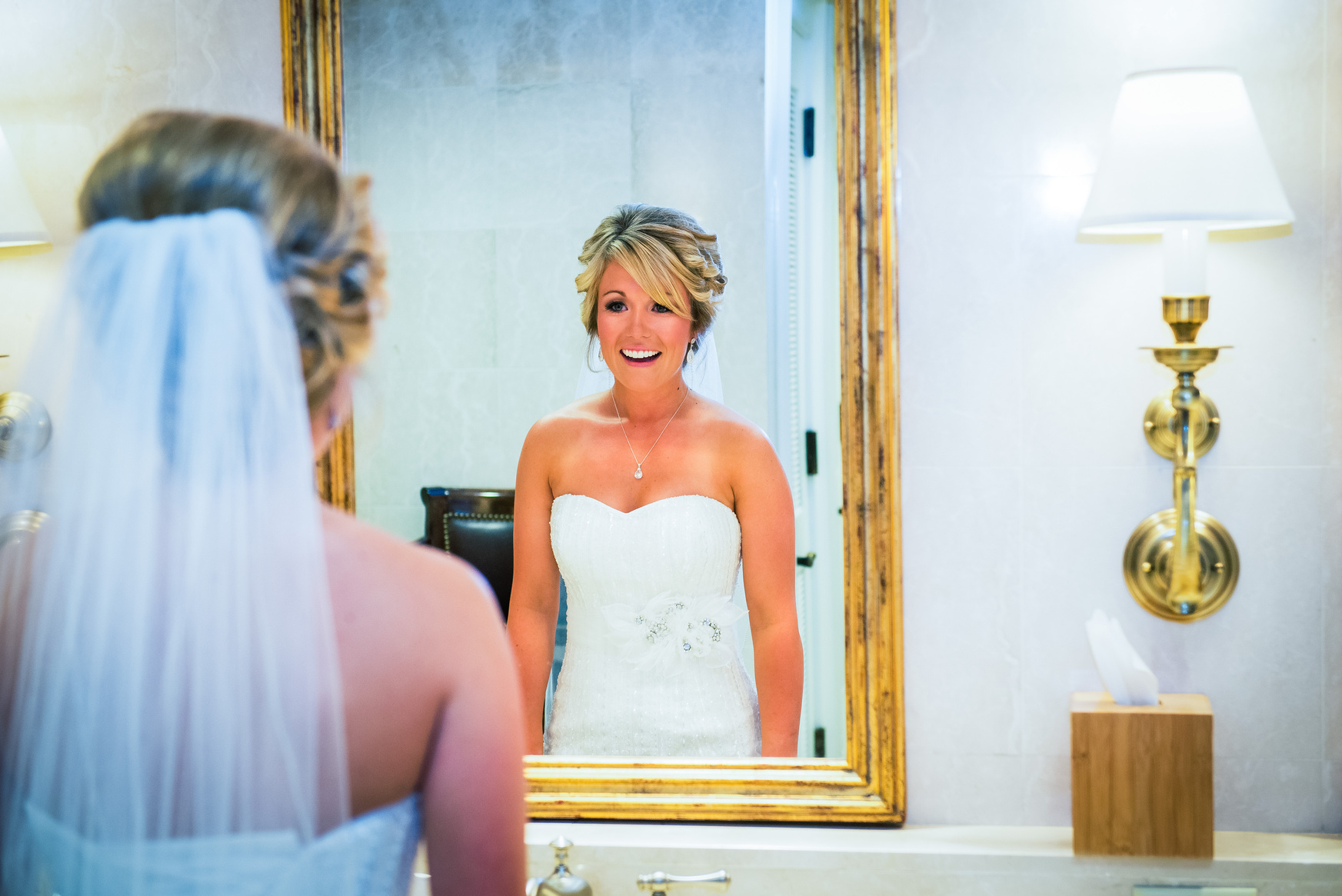 A bride in a wedding dress is looking at herself in a gold mirror.