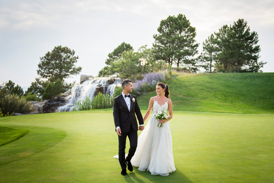 A bride and groom hold hands and walk toward the camera at a Colorado golf course wedding venue.