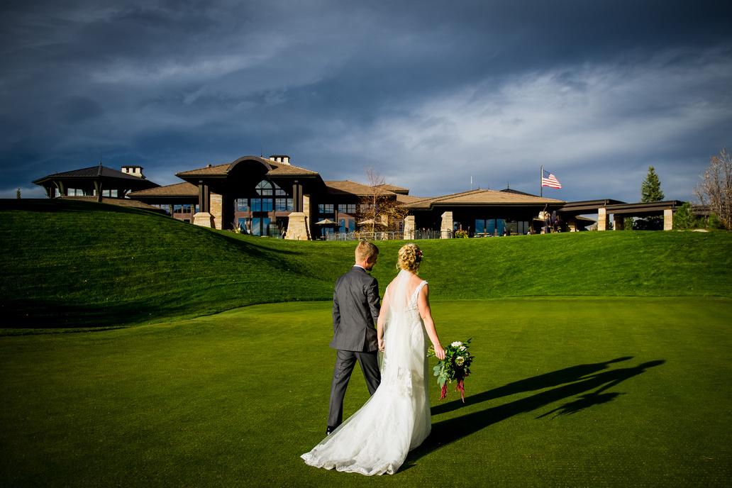 A bride and groom walking on the golf course at The Sanctuary with the building and stormy sky in the background.