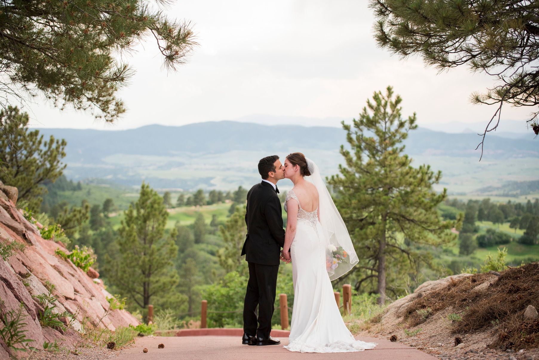 A bride and groom share a kiss while walking along a path with Colorado mountains in the background.