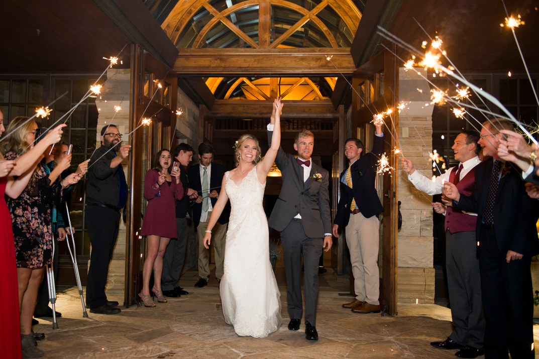 A bride and groom exit the reception hand-in-hand with their guests holding sparklers.